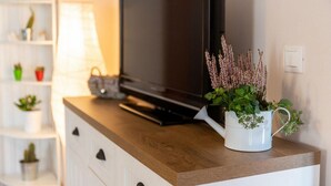 Una sala moderna con un televisor de pantalla plana sobre un mueble de madera, una taza blanca con plantas y un estante blanco con adornos.