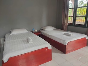 A room with two single beds, each with a red base and white bedding. There is a small table with a bottle and a tissue box on it. - Leokhamphasurt Resort (Thalat)