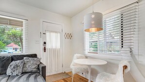 A modern living room with a gray sofa, white chairs, a round table, and a large window with blinds. - Sophies Cottage (Colorado Springs)