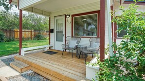 A covered porch with a wooden deck, two wicker chairs, and a bench. - Sophies Cottage (Colorado Springs)