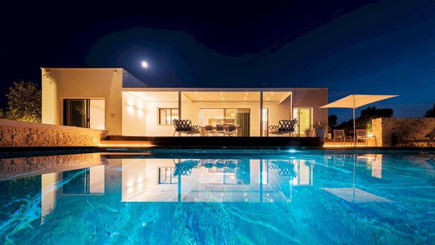 Una casa moderna con piscina, ventanas amplias y mobiliario exterior.