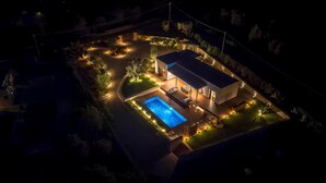Vista aérea de una casa moderna con piscina, rodeada de senderos iluminados y un jardín ajardinado.
