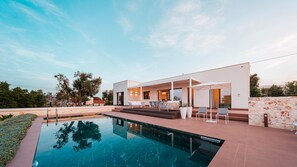A modern house with a swimming pool, outdoor seating, and a stone wall.
