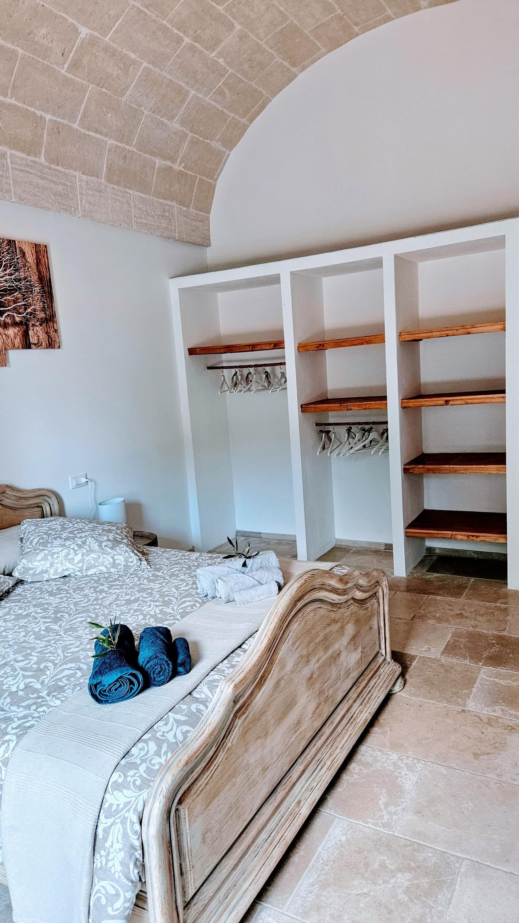 Ein Schlafzimmer mit einem Bett, einem Holzkopfende, einem weißen Kleiderschrank mit Regalen und einer Kleiderstange.
