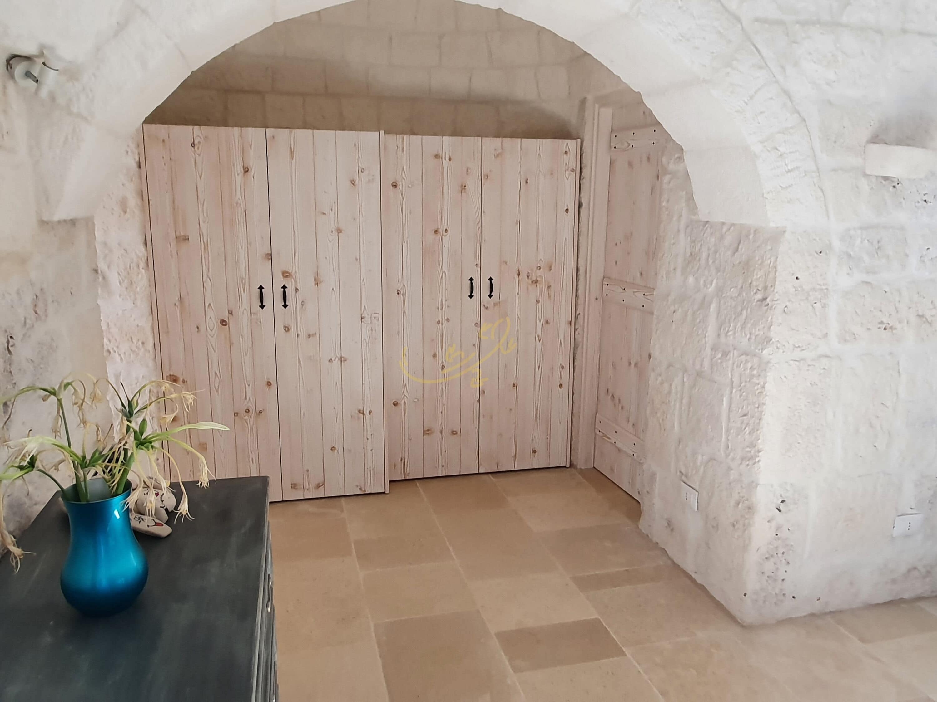 Una habitación con pared de piedra blanca, puerta de madera y suelo de baldosas.