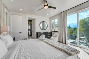 A bedroom with a large bed, a ceiling fan, a mirror, a dresser, and a balcony with outdoor furniture. - Elevated View (Colorado Springs)