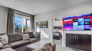 A modern living room with a large flat-screen TV displaying streaming services, a sofa set, and a view of the outdoors. - Elevated View (Colorado Springs)