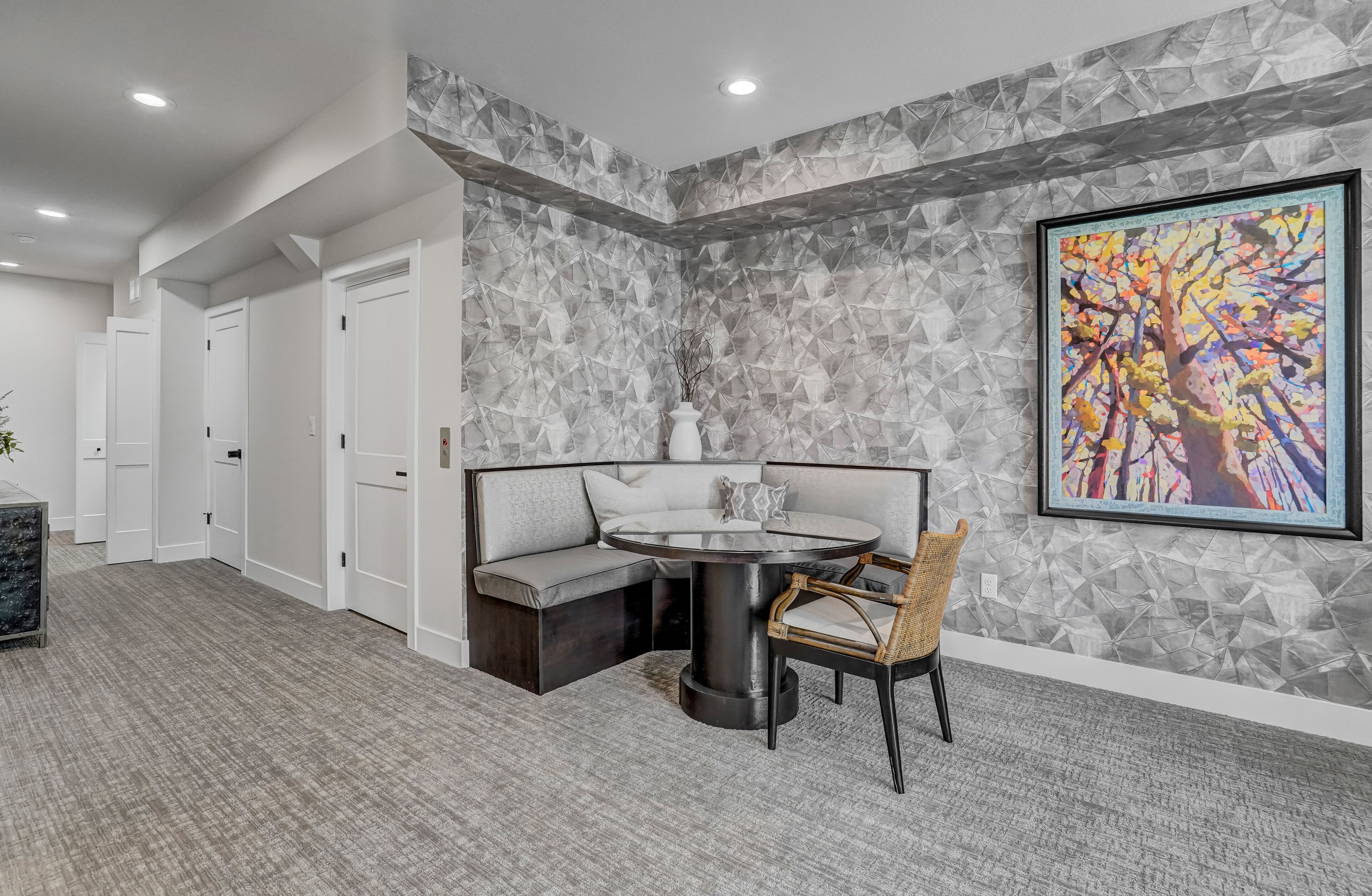 A modern interior with a round table and a cushioned bench, a geometric wall design, and a framed abstract painting.