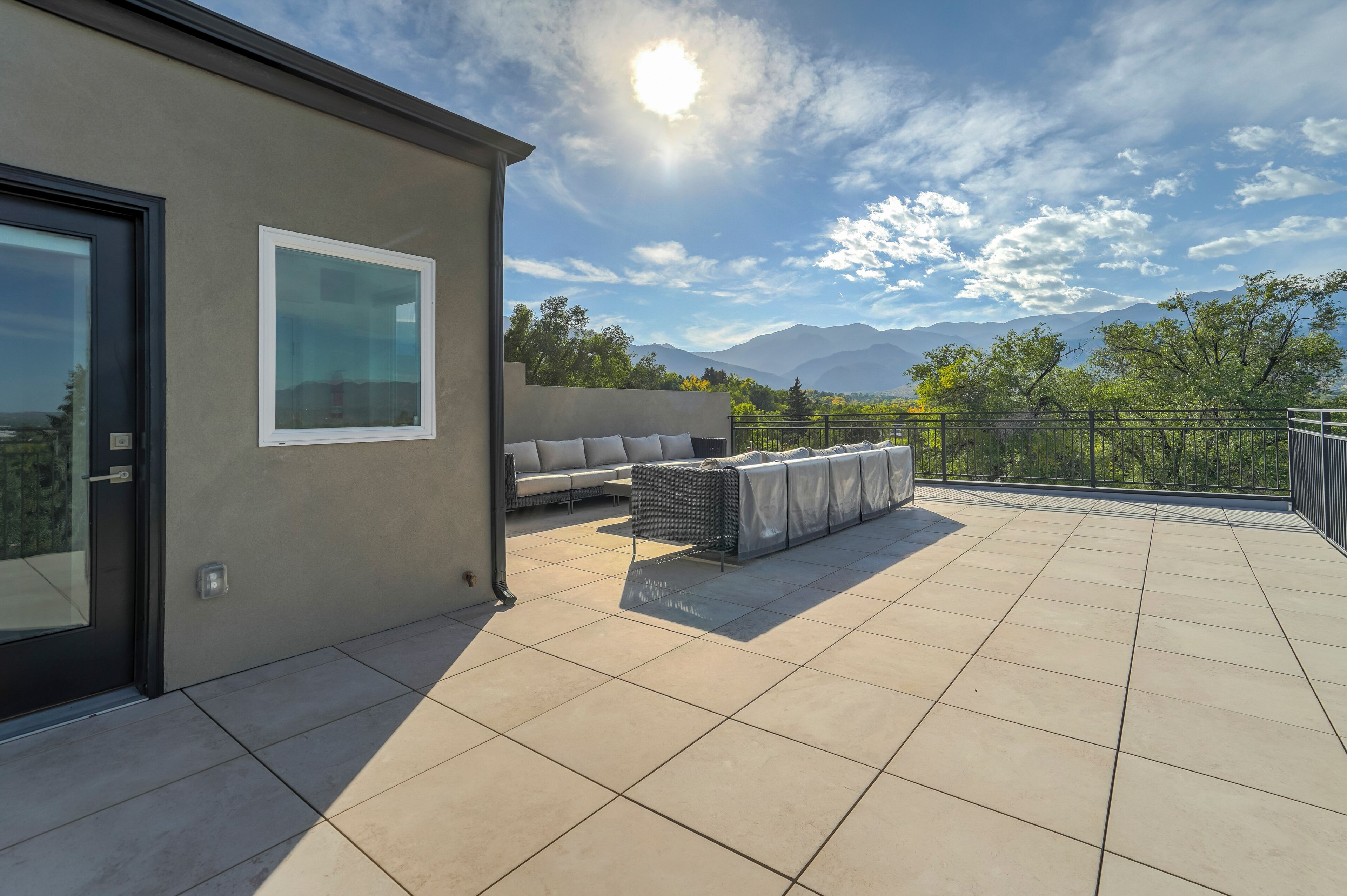 A modern outdoor patio with a sofa and a covered table, a glass door, and a view of mountains.
