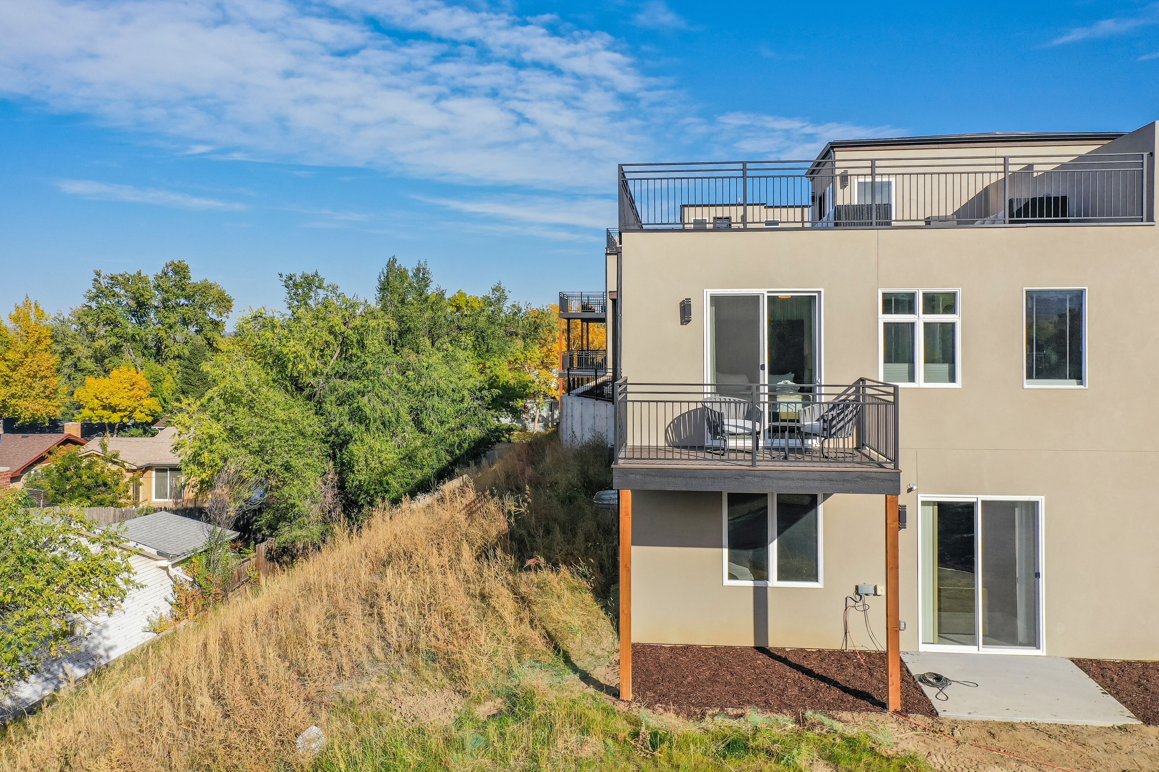 A modern two-story building with a balcony, large windows, and a view of surrounding trees.