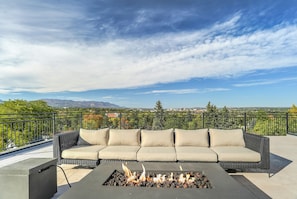 A rooftop terrace with a black metal railing, a beige sofa with cushions, and a built-in fire pit.