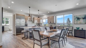 A modern kitchen with a central island, pendant lighting, and a dining area with a wooden table and chairs. - Elevated View (Colorado Springs)