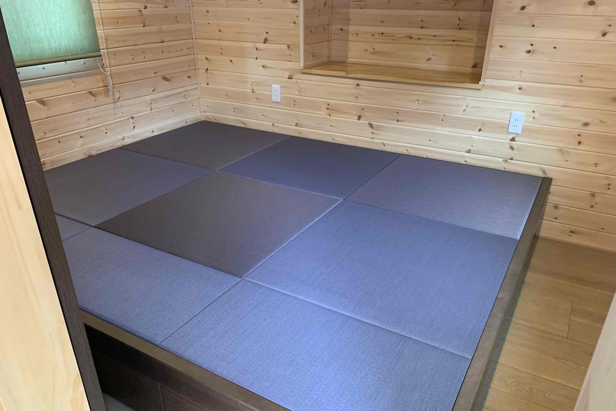 A room with a wooden floor and a large, dark-colored mat covering the floor.