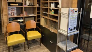 A room with wooden shelving, a vending machine, and two yellow chairs. - Kita-alps BASE Onsenkyo Camp (Omachi)