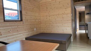 A compact room with wooden walls, a small window, a table, and a bench. - Kita-alps BASE Onsenkyo Camp (Omachi)