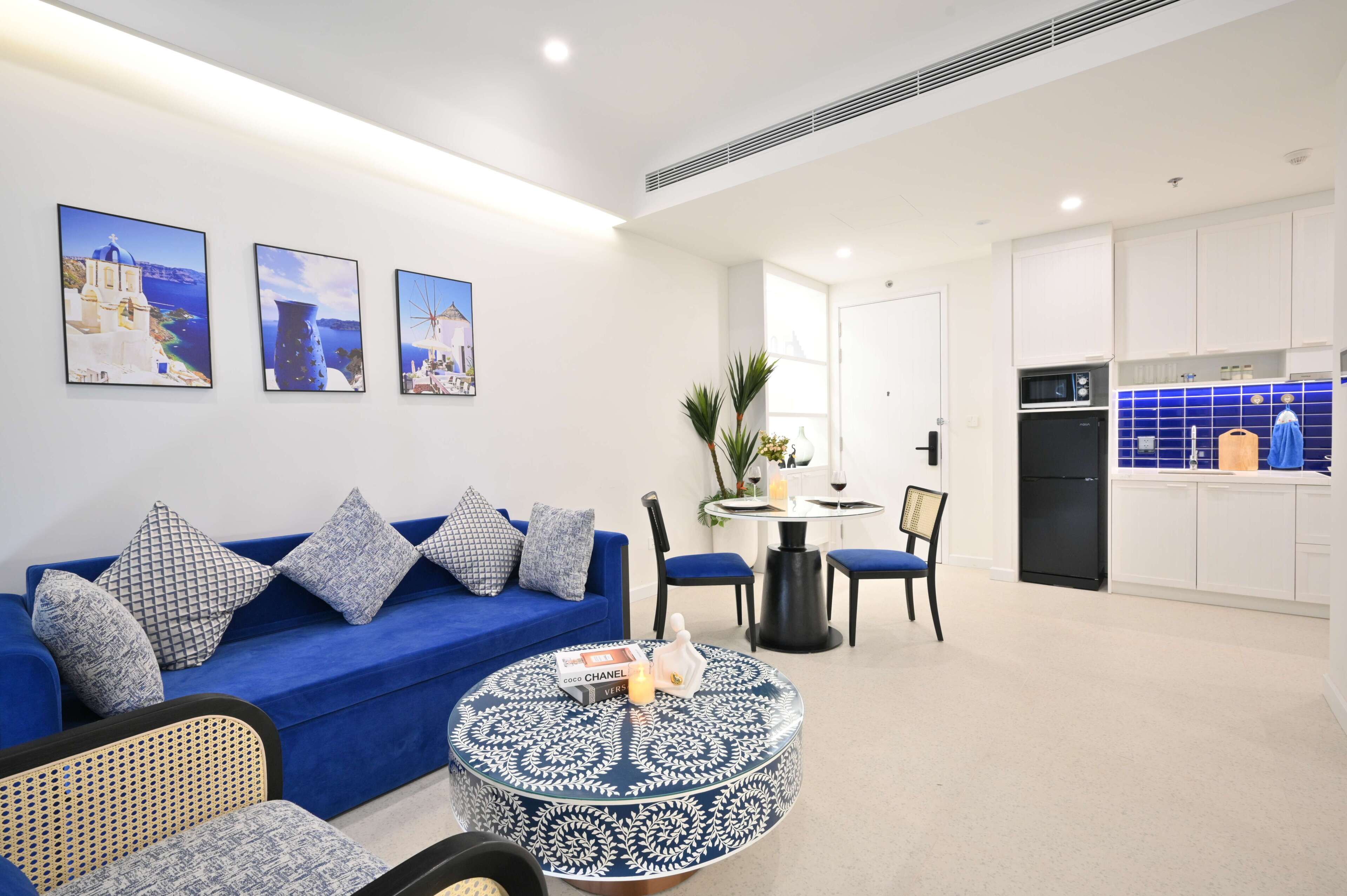 Een moderne woonkamer met een blauwe bank, een ronde salontafel en een eetgedeelte met een kleine tafel en stoelen.