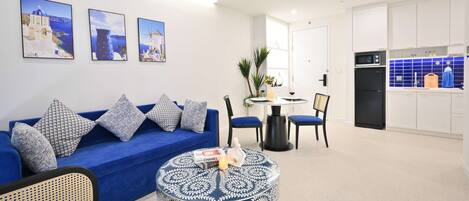 Een moderne woonkamer met een blauwe bank, een ronde salontafel en een eetgedeelte met een kleine tafel en stoelen.