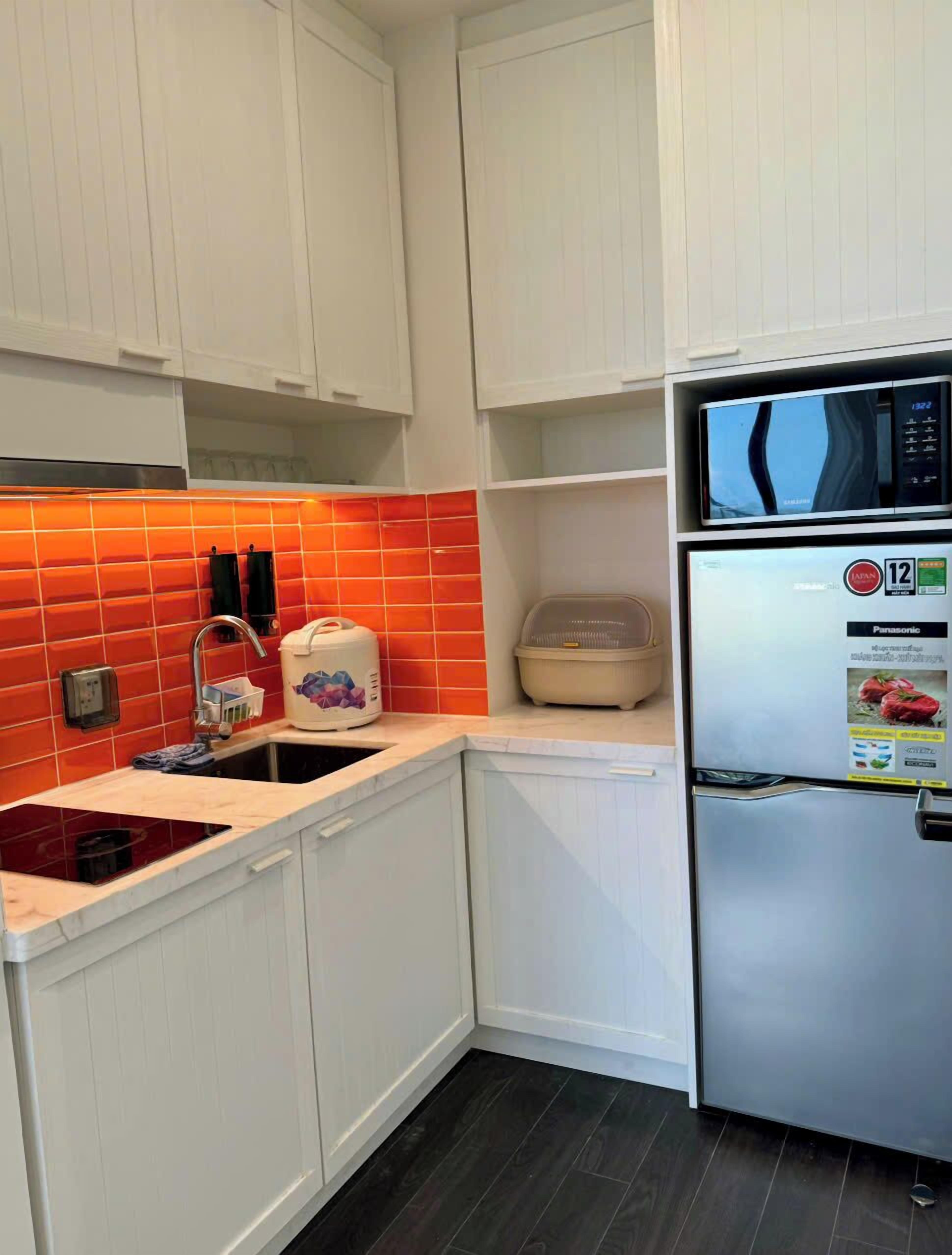 Een keuken met witte kastjes, een rode tegelachtergrond, een roestvrijstalen koelkast en een magnetron.
