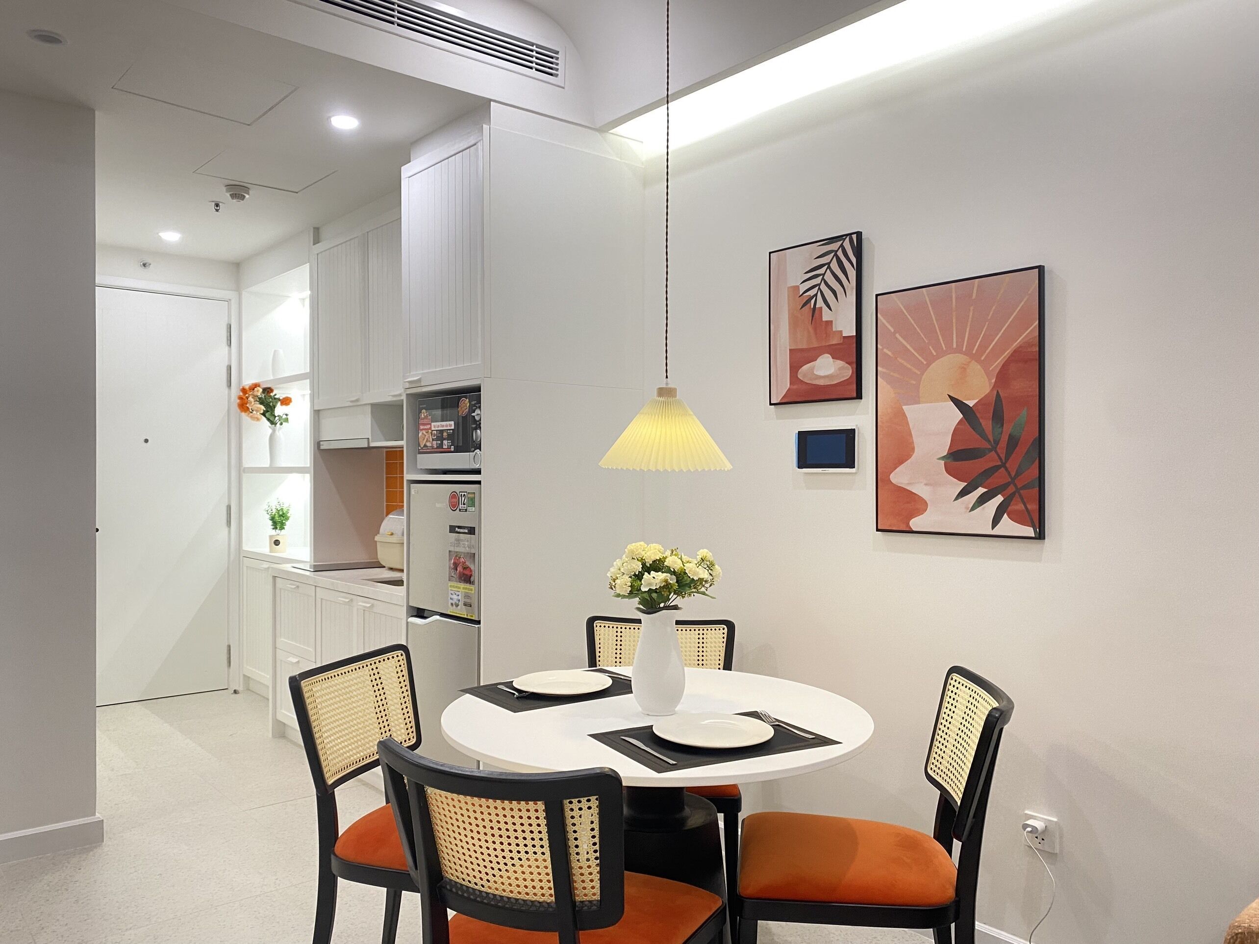 A modern dining area with a round table, four chairs, a vase with flowers, and wall art.