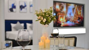 A dining table with candles, wine glasses, and a vase of flowers. A bed and a television are visible in the background.