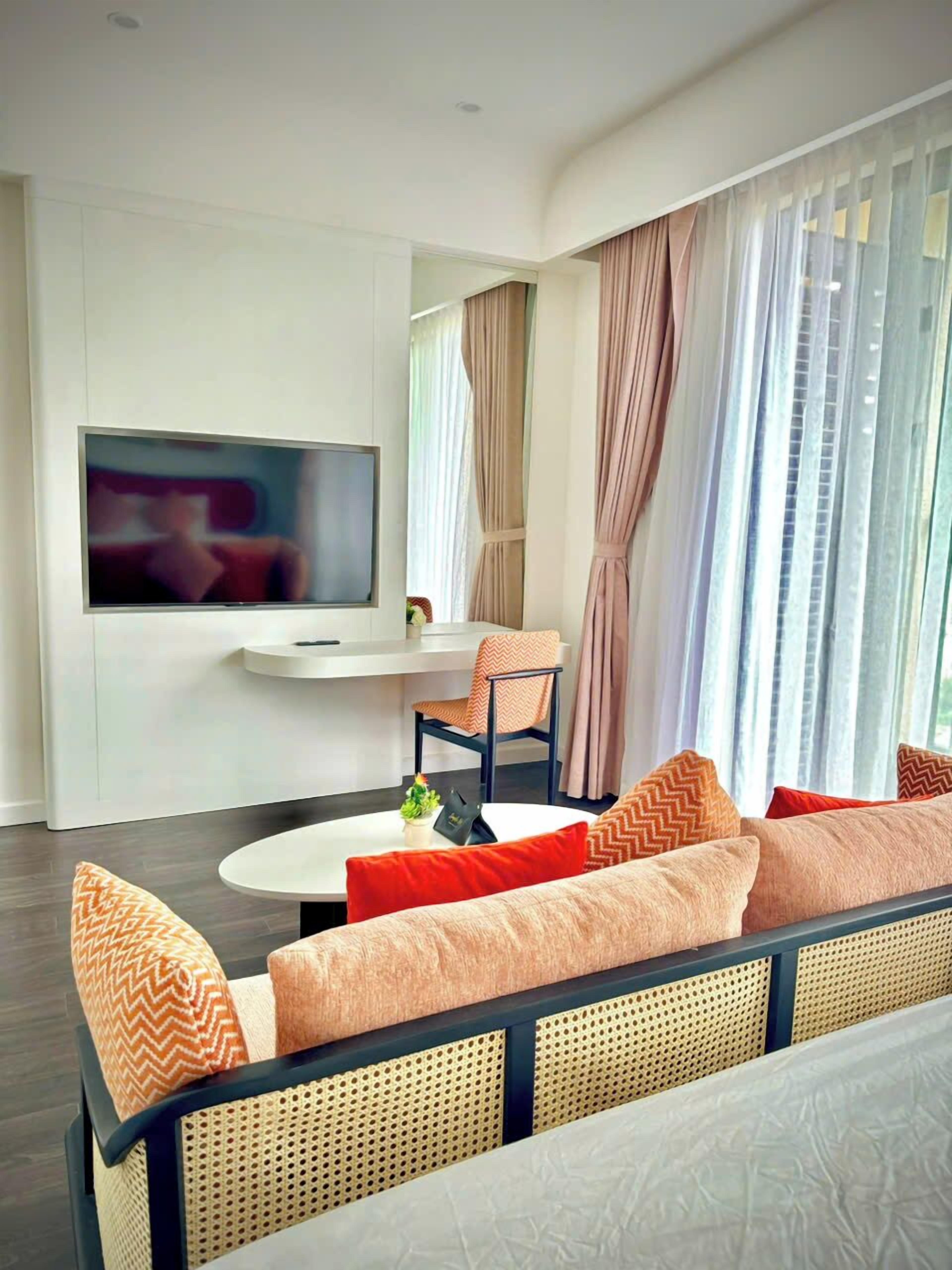 Een moderne woonkamer met een bank, een salontafel, een aan de muur bevestigde televisie en een groot raam met gordijnen.
