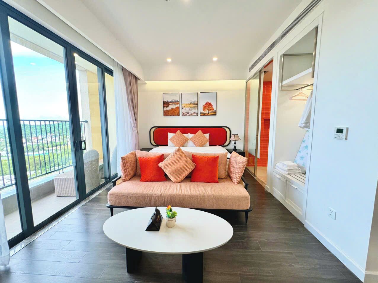 A modern hotel room with a large bed, a sofa, a round coffee table, and a balcony with a view.