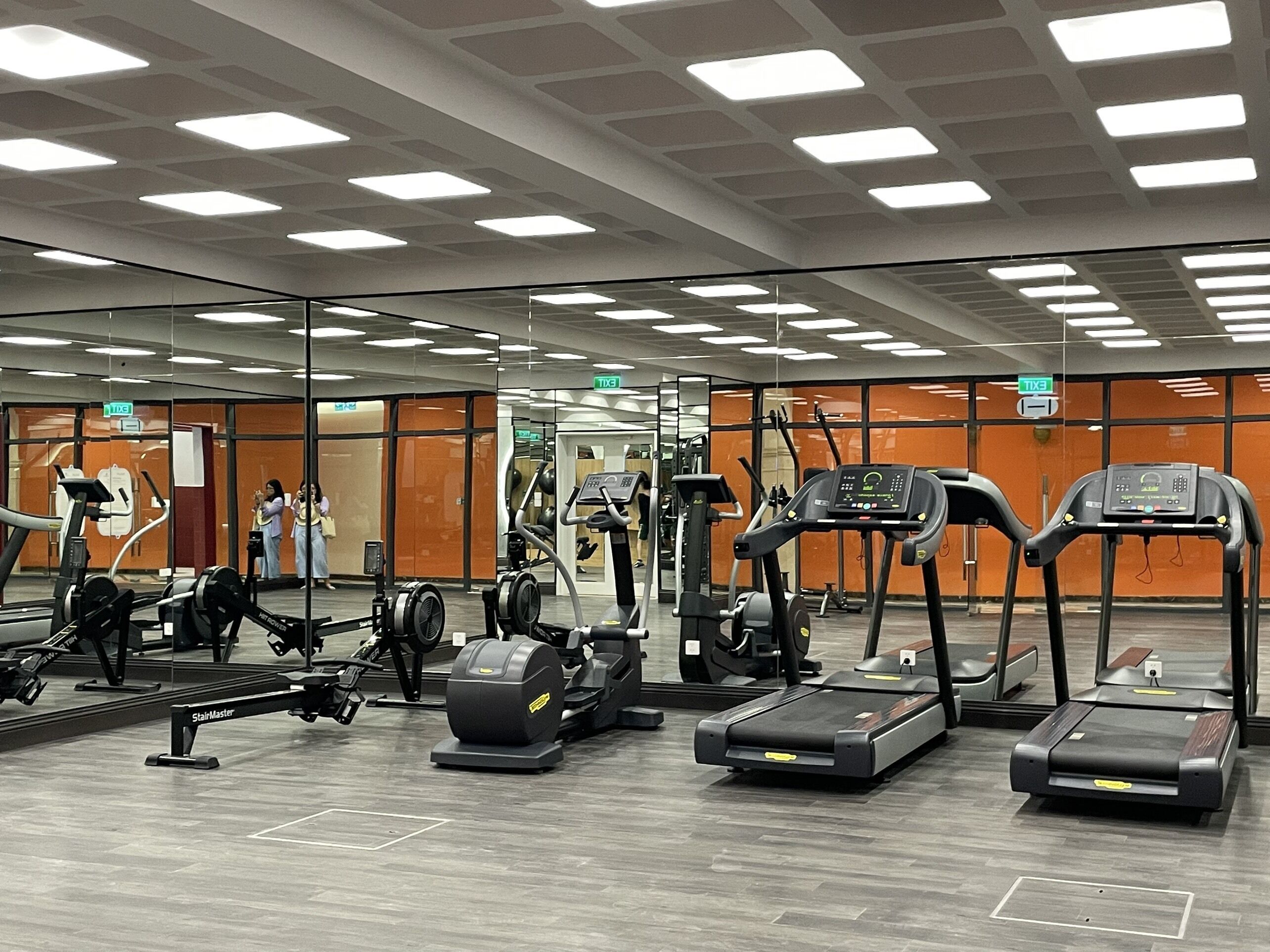 A gym with various exercise equipment, mirrored walls, and a wooden floor.
