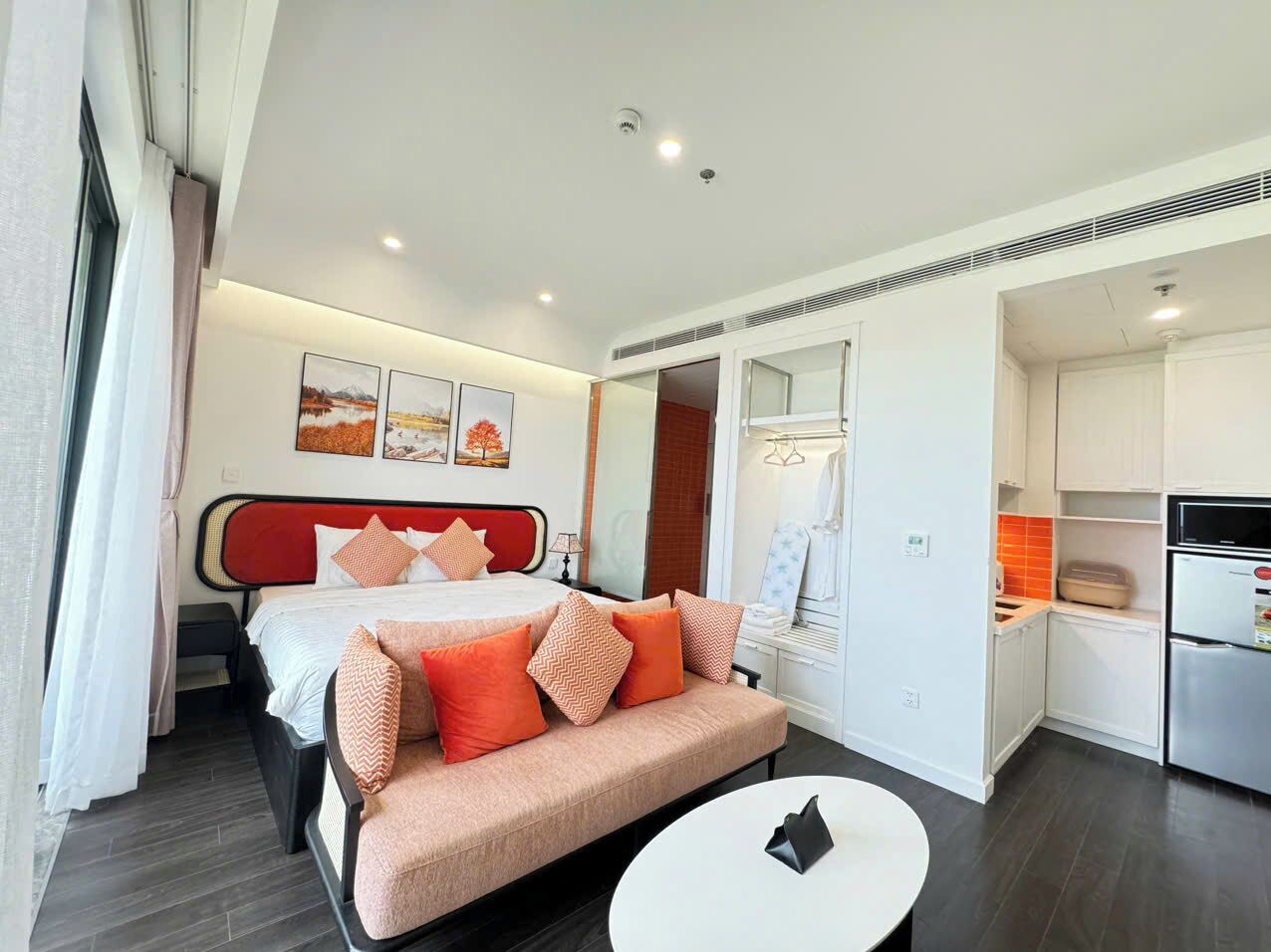 A modern hotel room with a bed, a sofa, a small dining table, and a kitchenette.