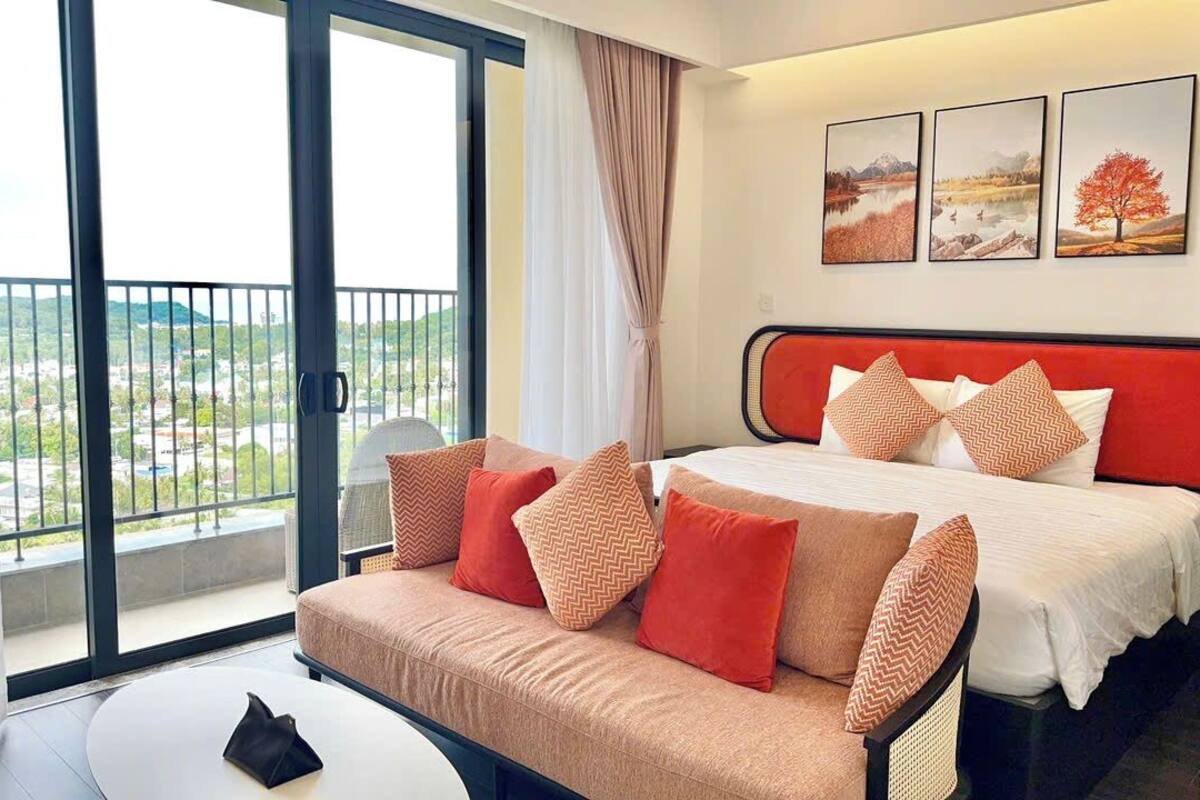 Een hotelkamer met een bed, een slaapbank, een balkon met uitzicht en drie ingelijste foto’s aan de muur.