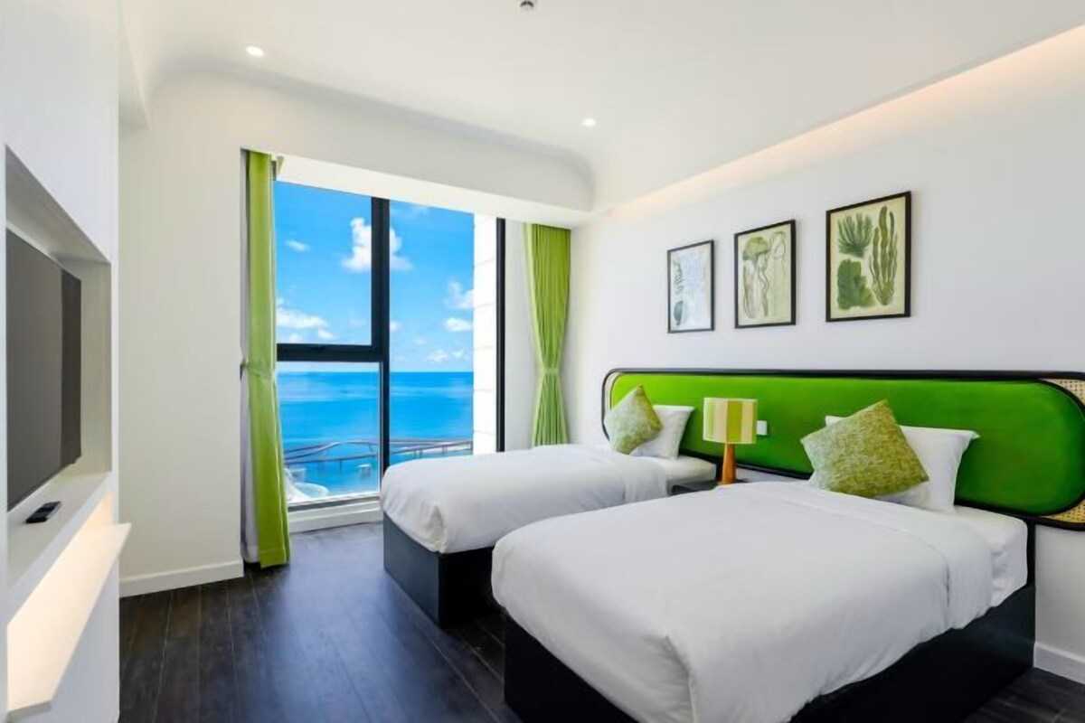 A hotel room with two beds, a large window with a view of the ocean, and artwork on the wall.