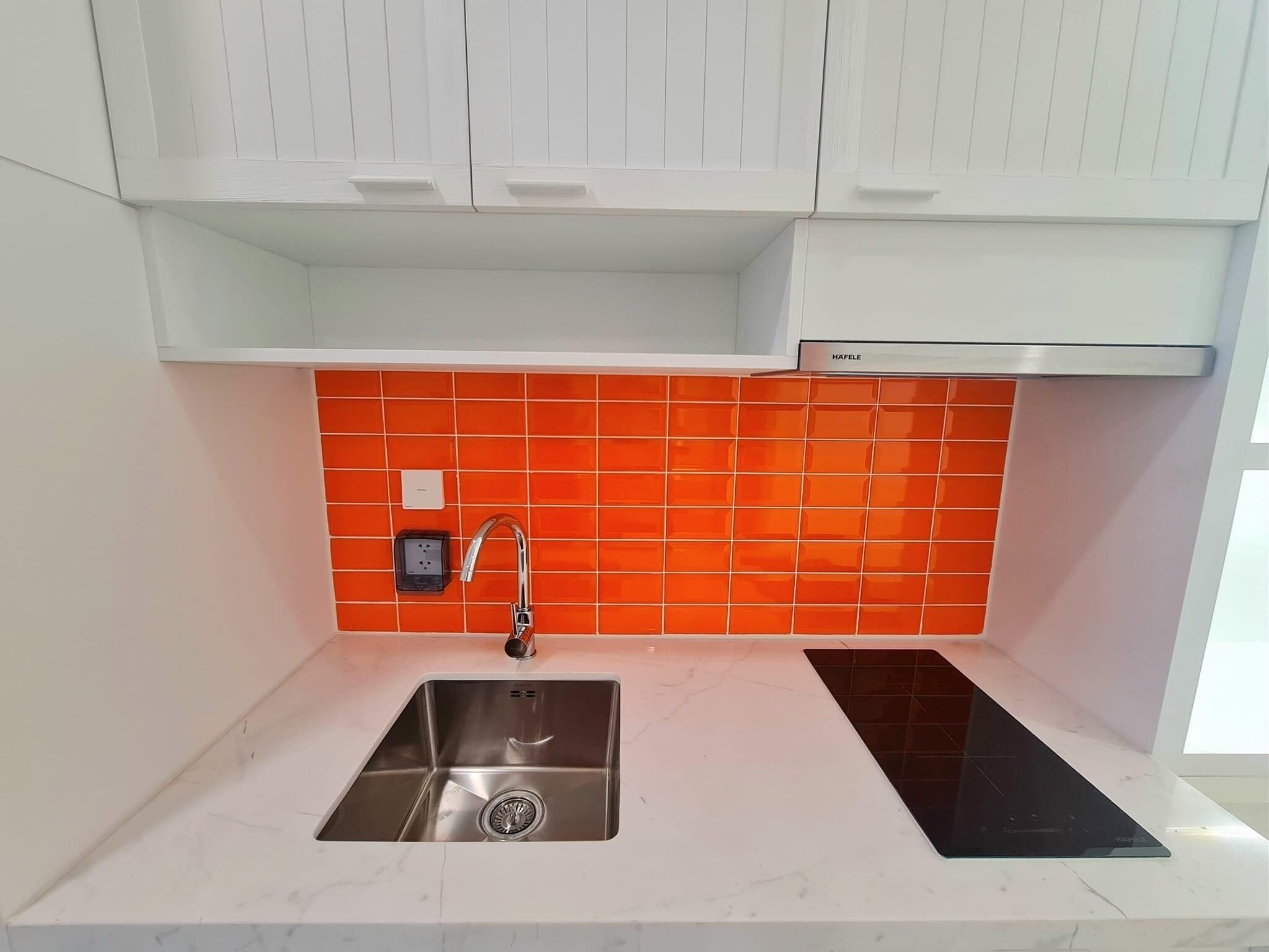 A kitchen with a stainless steel sink, a black induction cooktop, and white cabinets.