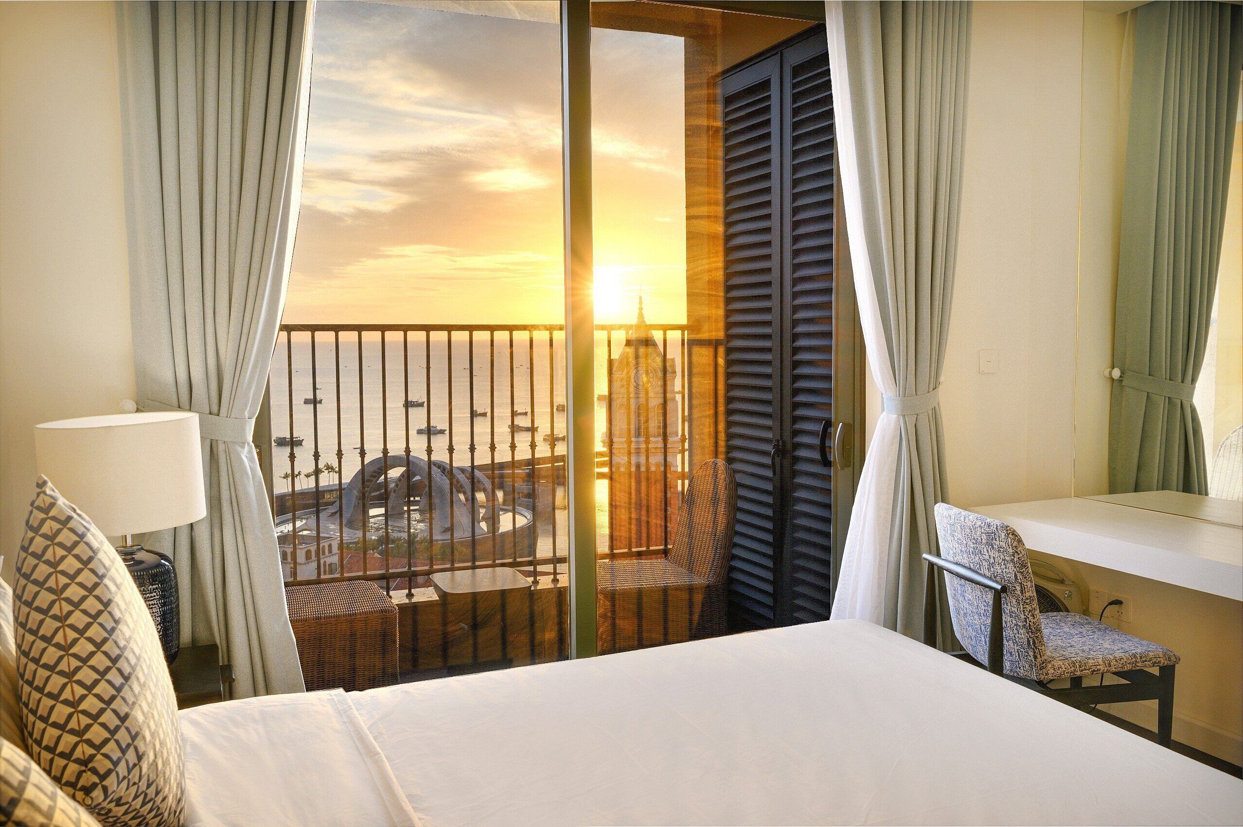 Een hotelkamer met balkon, bed, stoel en tafel.