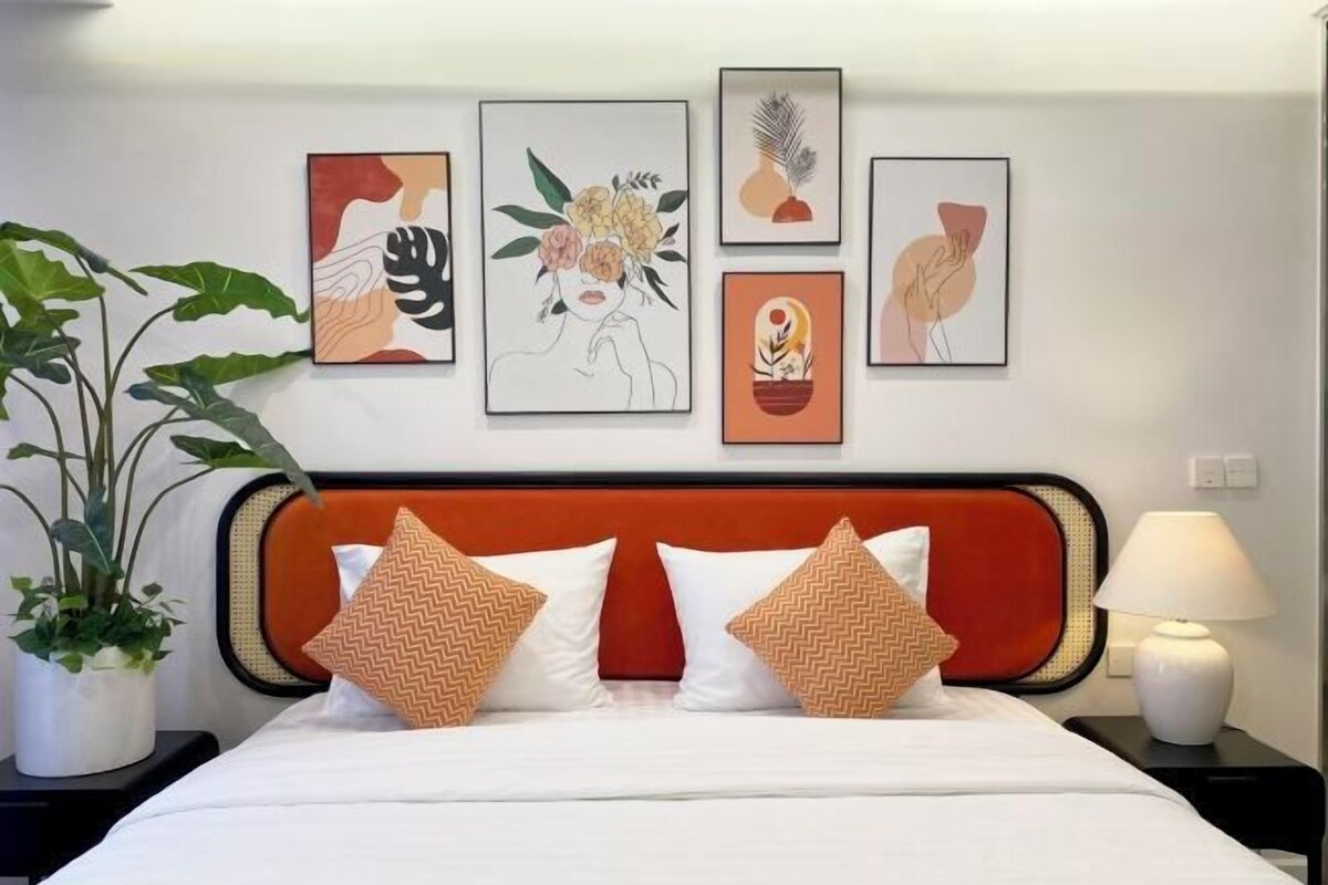 A hotel room with a bed, a nightstand, a lamp, and four framed artworks on the wall.