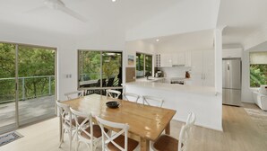 A modern kitchen with white cabinets, a stainless steel refrigerator, and a dining area with a wooden table and white chairs. - Villa Luna (Avoca Beach)