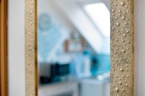 Un espejo con un marco de textura perlada, que refleja una habitación con pared azul y techo blanco.