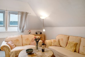 Una habitación acogedora con un sofá, una mesa con un jarrón y copas de vino, una lámpara y un radio.