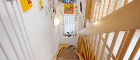 Un escalier avec des rampes en bois, des marches recouvertes de moquette et diverses décorations murales, notamment des tableaux encadrés et une peinture de dragon.