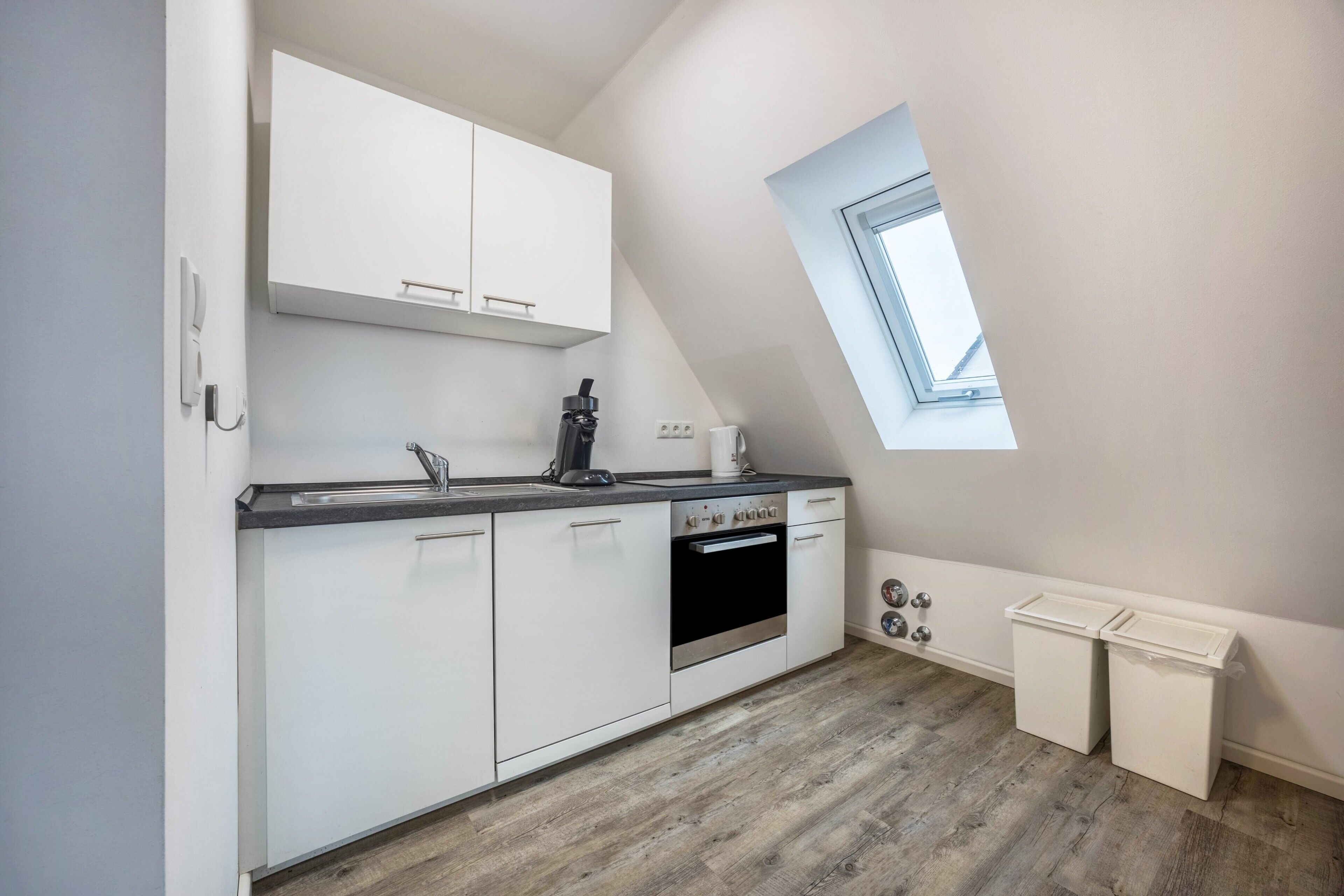 A modern kitchen with white cabinets, a built-in oven, and a skylight.