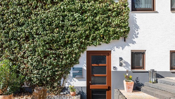 A building with a white exterior, a brown door, and a large ivy-covered wall. - Holiday Apartment "Kirchheim" with Private Terrace, Private Garden and Wi-Fi (Kirchheim)