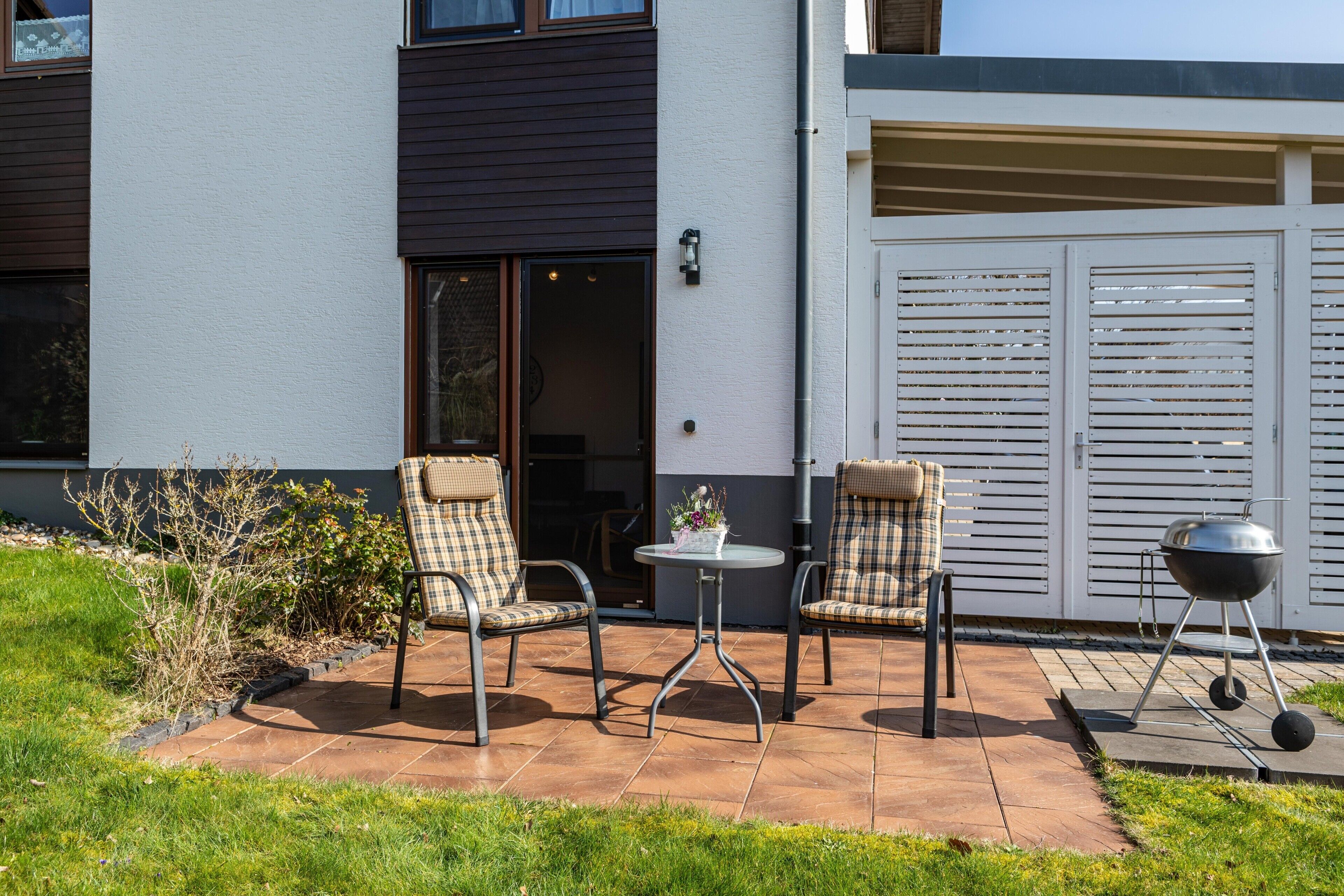 Een terras met twee stoelen, een kleine tafel en een barbecue.