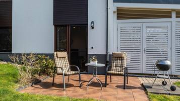 Een terras met twee stoelen, een kleine tafel en een barbecue.