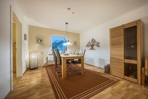 Ein Essbereich mit Tisch, Stühlen, einer Hängelampe, einem Fenster und einem Holzschrank.
