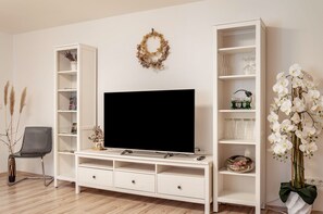 Una sala de estar con un televisor de pantalla plana, estanterías blancas, un adorno decorativo y una orquídea en maceta.