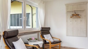 Ein Zimmer mit zwei Ledersesseln, einem kleinen Tisch mit einer Schale und einem rosa Teelicht, einem Heizkörper und einem Fenster mit Vorhängen.
