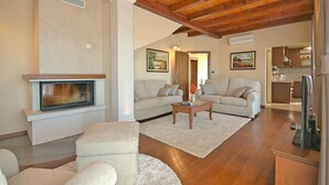 A living room with a fireplace, two sofas, a coffee table, and a kitchen area visible through an open door.