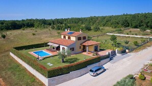 A two-story house with a swimming pool, a car parked in front, and a well-maintained garden.