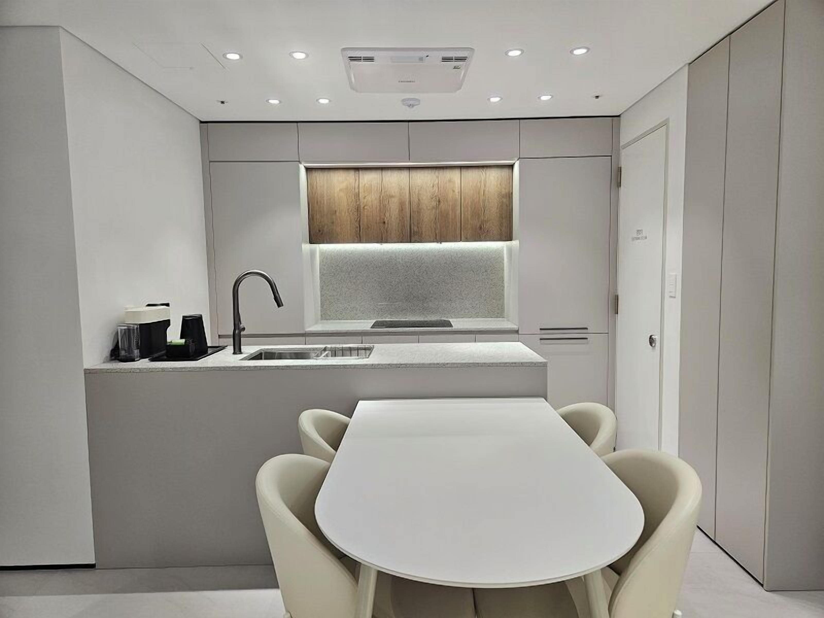 A modern kitchen with a built-in island, a window above the sink, and a dining area with a white table and chairs.