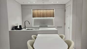 Een moderne keuken met een vast kookeiland, een raam boven de gootsteen, en een eethoek met een witte tafel en stoelen.