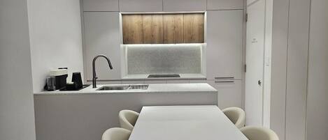 A modern kitchen with a built-in island, a window above the sink, and a dining area with a white table and chairs.