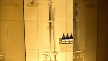 A bathroom with two showerheads, a hand dryer, and a shelf with bottles.